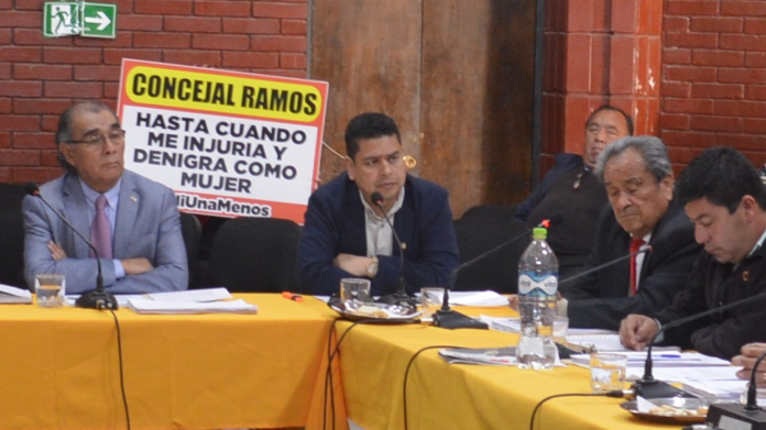 Detrás del mismo concejal Carlos Ramos, armada con un cartel y en plena sesión del concejo municipal, Daniela Huerta protestó en contra de la autoridad por supuestas ofensas e injurias que éste vendría realizando contra ella.